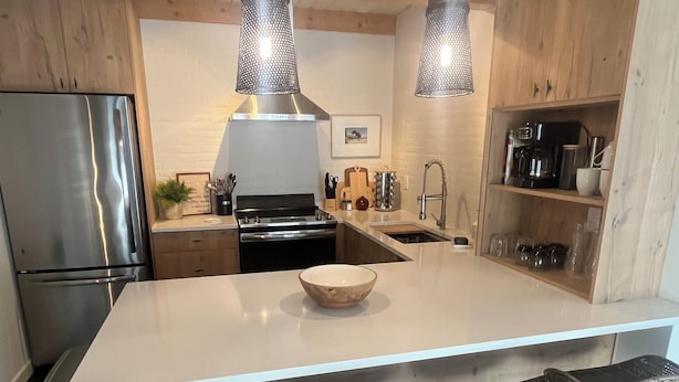 Una cocina moderna con una isla central, electrodomésticos de acero inoxidable, lámparas colgantes y techo de madera.