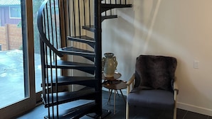 Un interior moderno con una escalera en espiral, una zona de estar y vistas amplias a través de un gran ventanal.