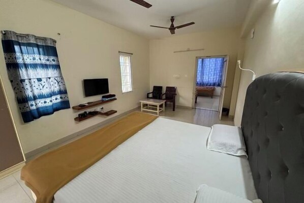 A hotel room with a bed, a television, a ceiling fan, a window, and a small table. - Srinivasa Hotel (Chittoor District)