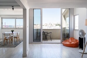 Un appartement moderne doté d’un coin repas, d’un balcon offrant une vue sur la ville et d’un espace salon confortable.