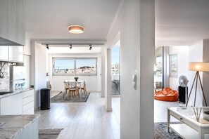Una cocina moderna con armarios blancos, encimera de mármol y zona de comedor con mesa y sillas.