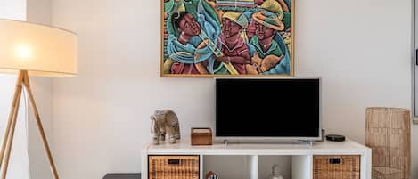 A room with a television on a white stand, a lamp, and a decorative elephant figurine.