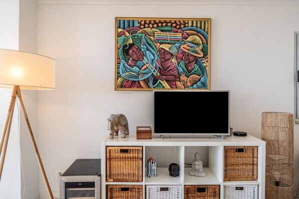 Une pièce avec un téléviseur posé sur un meuble blanc, une lampe et une statuette d’éléphant décorative.