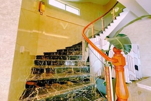 A marble staircase with a glass railing, a wooden handrail, and a large plant at the bottom. - Haiyun Hotel (Dongshan Island Jinluan Bay Scenic Area) (Dongshan County)