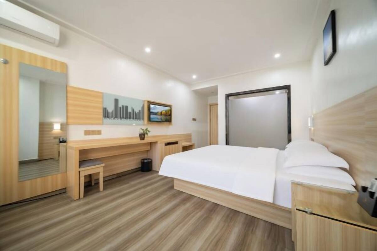 Una habitación de hotel moderna con una cama grande, un escritorio de madera, una silla, una mesita pequeña, un espejo y un cuadro en la pared.