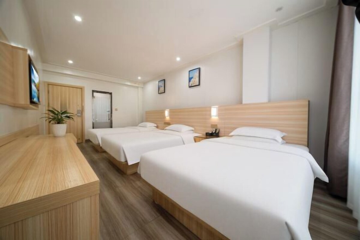 A hotel room with three beds, a wooden desk, and a potted plant.