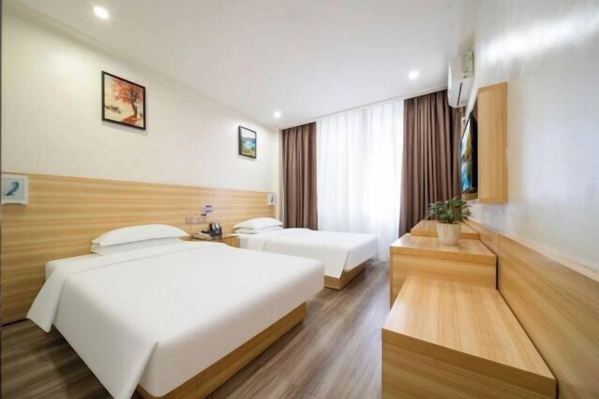 Habitación de hotel con dos camas, un banco de madera, una mesita y un televisor montado en la pared.
