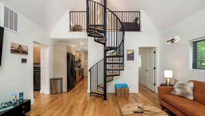 Un salon moderne avec un escalier en colimaçon, un plancher en bois, un canapé, une table basse et une cuisine en arrière-plan.