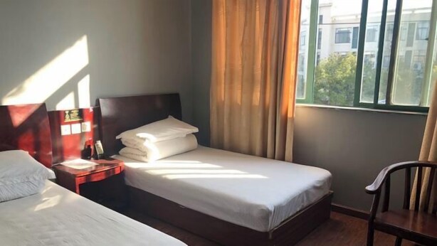 Quarto de hotel com duas camas, uma mesinha de cabeceira, uma cadeira e uma janela com cortinas.