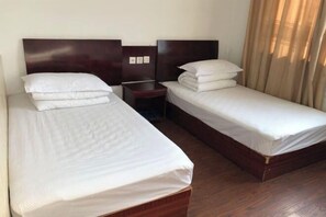 A hotel room with two single beds, a wooden headboard, a bedside table, and a nightstand.