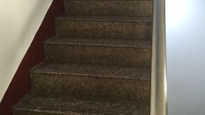 Uma escadaria com corrimão e uma parede vermelha de um lado.