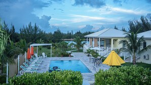 Un espace piscine avec des chaises longues, un parasol jaune et une vue sur l’océan.