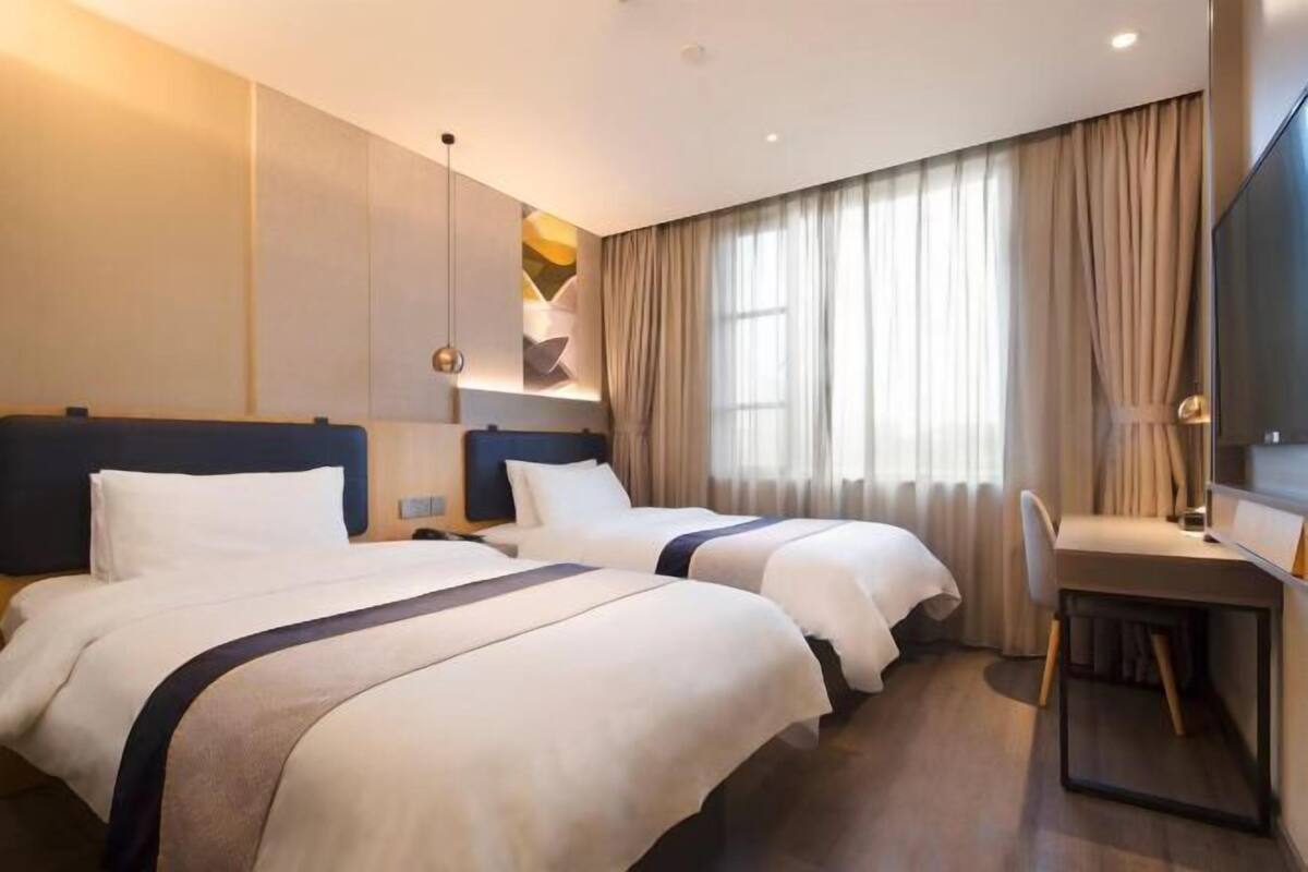 Een hotelkamer met twee bedden, een bureau en een groot raam met gordijnen.