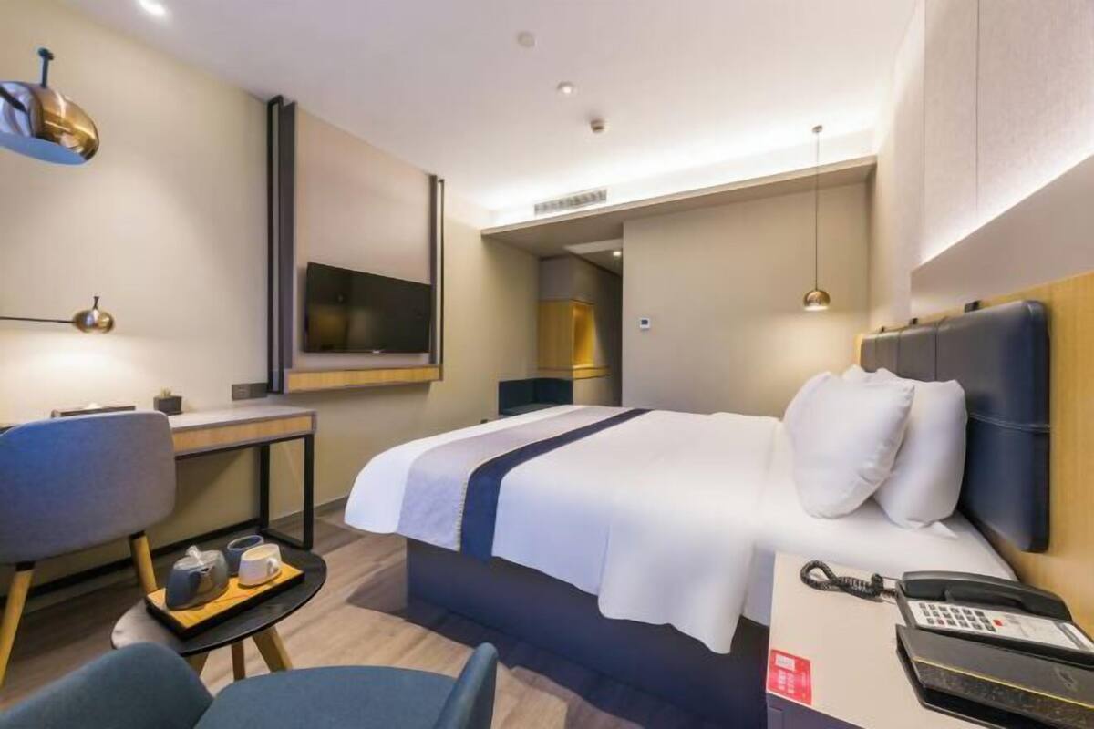 Een hotelkamer met een bed, een bureau, een stoel, een nachtkastje met telefoon en een televisie.