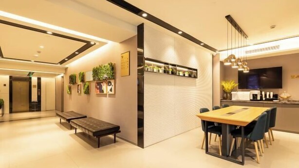 A modern hotel lobby with a wooden dining table and benches, a reception desk, and a wall-mounted plant display. - Homeinn Selected Hotel (Shanghai Convention Center Qibao Metro Station) (Shanghai)