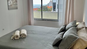 A bedroom with a large bed, a view of the city, and a painting on the wall. - Lido Casa by Olá Madeira (Funchal)