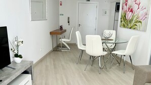 A modern living room with a TV, white chairs, a glass table, and a beige sofa. - Lido Casa by Olá Madeira (Funchal)