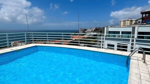 A clear blue swimming pool with a metal railing, surrounded by buildings and a clear sky. - Lido Casa by Olá Madeira (Funchal)