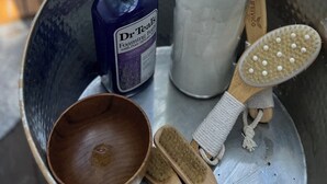 Ein Tablett mit einer Flasche Dr. Teals Foaming Bath, einem Behälter mit weißer Flüssigkeit, einer Holzbürste und einer Holztasse.