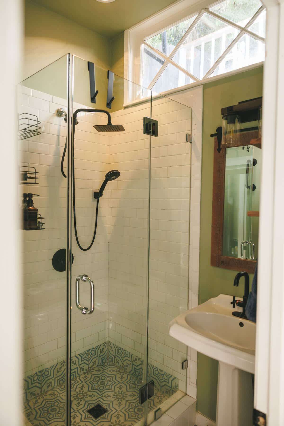 Une douche fermée par des parois en verre, dotée d’un pommeau de douche à main et d’un robinet à main.