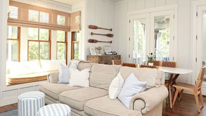 Un salon chaleureux avec un canapé beige, des poufs à rayures et des planches de surf en bois accrochées au mur.