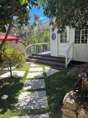 A white building with a blue and white sign, a stone pathway leading to a porch, and a red umbrella. - Two Room Garden Backyard: Zen Den + Farmhouse (Topanga)