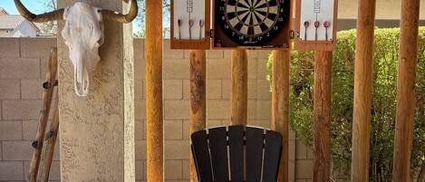 A dartboard mounted on a wooden structure with a bull skull decoration, a dartboard with a scorecard, and a black chair.