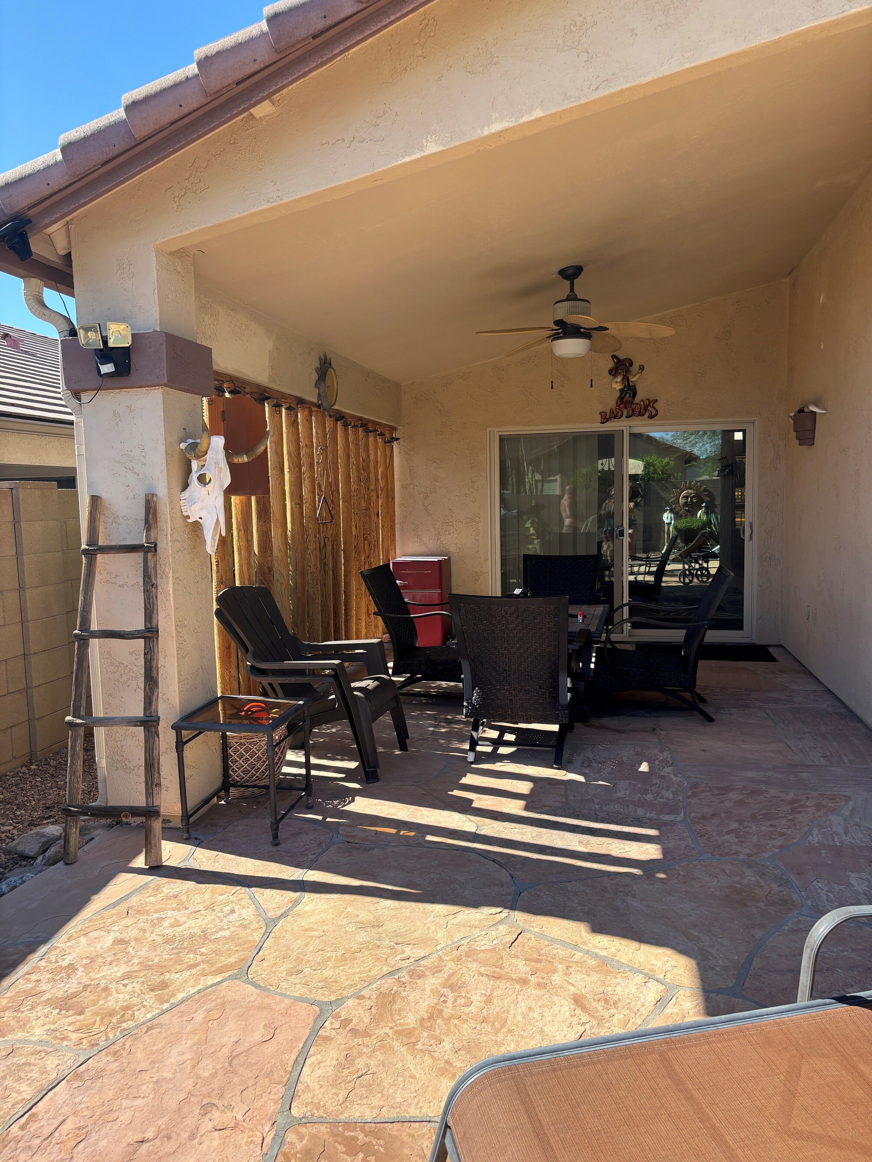 A covered patio area with stone flooring, a ceiling fan, and outdoor furniture.