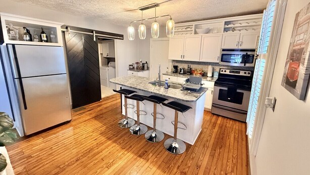A modern kitchen with a central island, bar stools, a refrigerator, a stove, and a microwave.