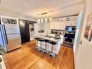 A modern kitchen with a central island, bar stools, a refrigerator, a stove, and a microwave. - Downtown House w/King Bed-Parking-Bars-Restaurants (Indianapolis)