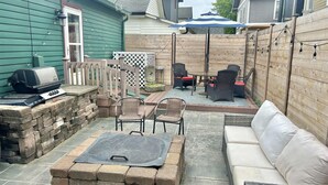 A backyard patio with a stone fire pit, outdoor furniture, and a barbecue grill.