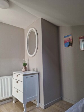 Une chambre avec une commode blanche, un miroir rond et deux tableaux encadrés accrochés au mur.