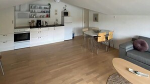 Une cuisine moderne avec des meubles blancs, un coin repas avec une table ronde et des chaises, et un canapé gris.