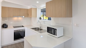 Una cocina moderna con armarios blancos, horno empotrado, pileta de acero inoxidable y microondas.