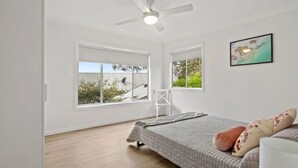Un dormitorio con cama, una silla y dos ventanas.