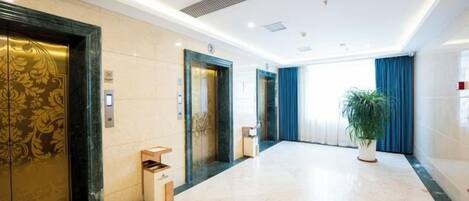 A hotel lobby with three elevators, a reception desk, and a potted plant.