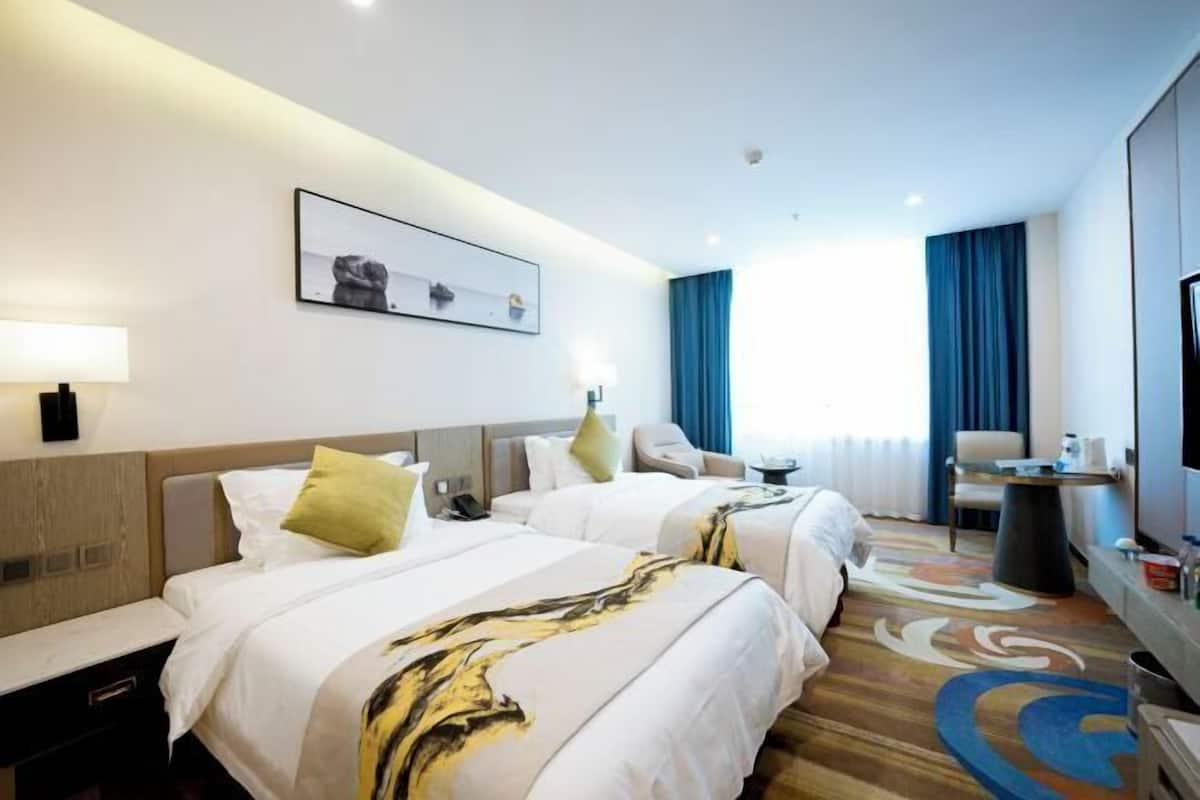 A hotel room with two beds, a desk, a chair, a TV, and a window with curtains.
