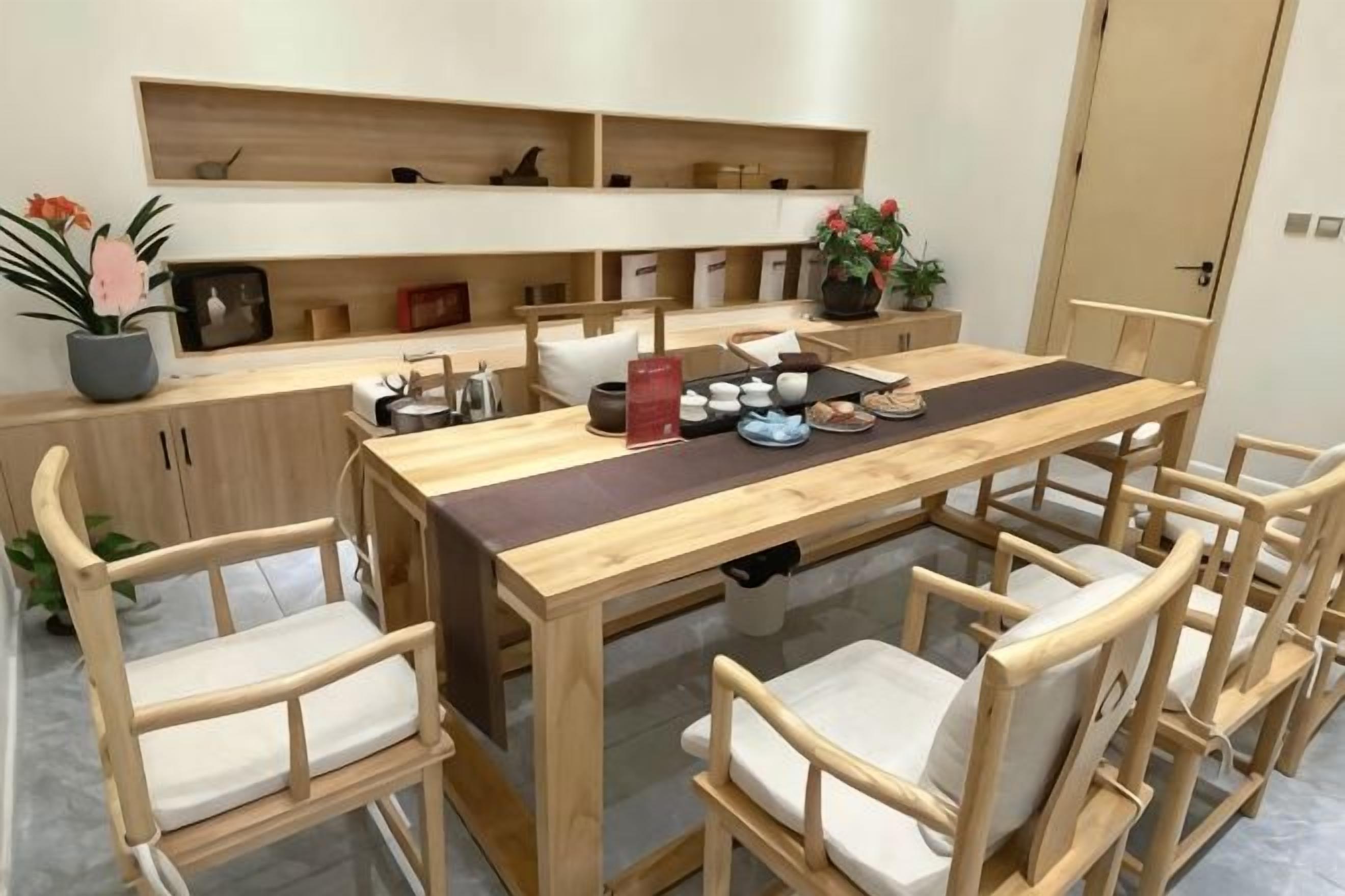 Un comedor con mesa y sillas de madera, una zona de cocina con estantes y una planta en maceta.