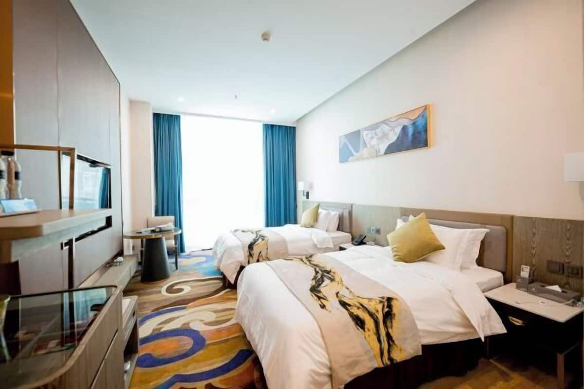 A hotel room with two beds, a desk, a chair, a TV, and a window with curtains.