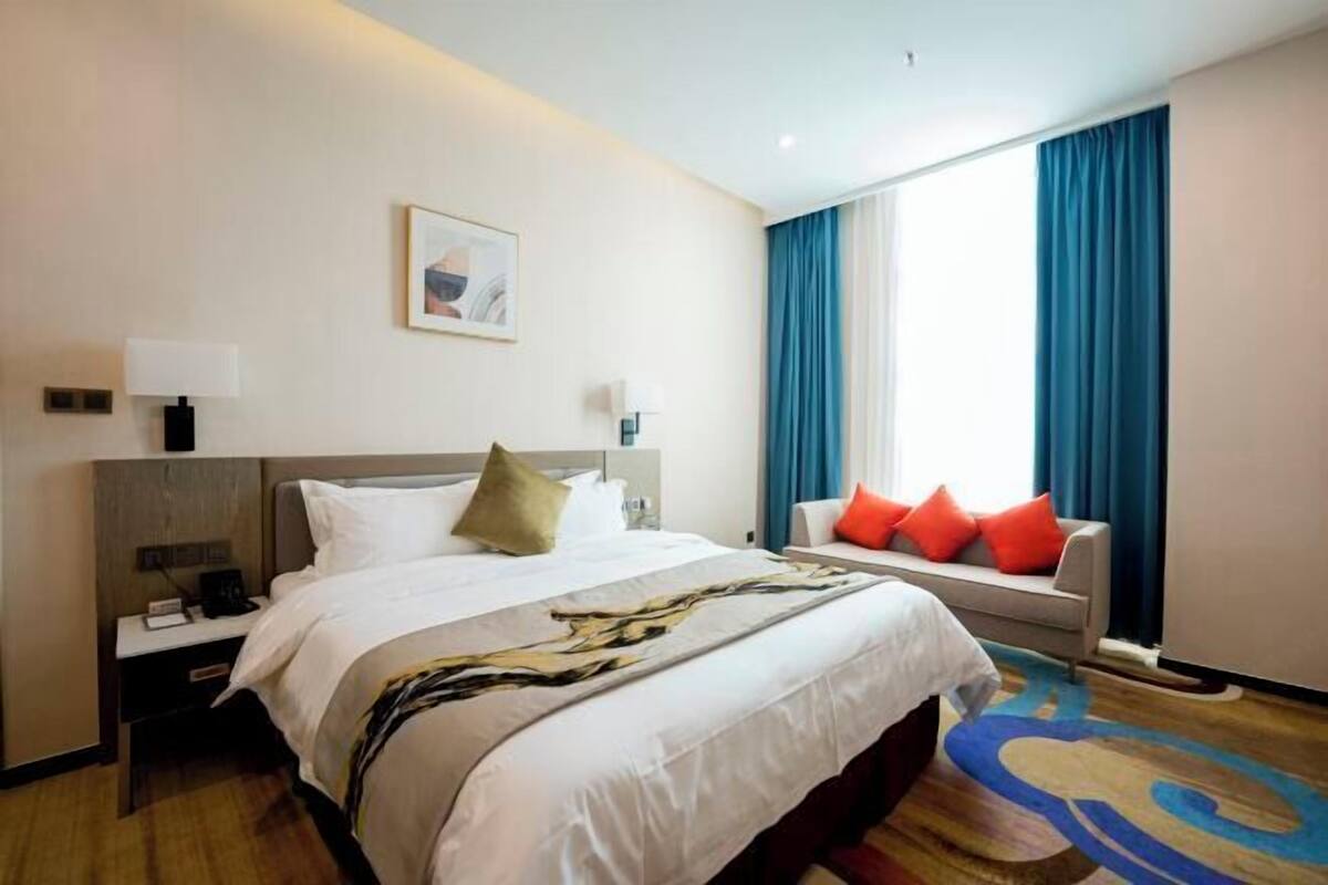 A hotel room with a large bed, a nightstand, a desk, a chair, and a window with curtains.