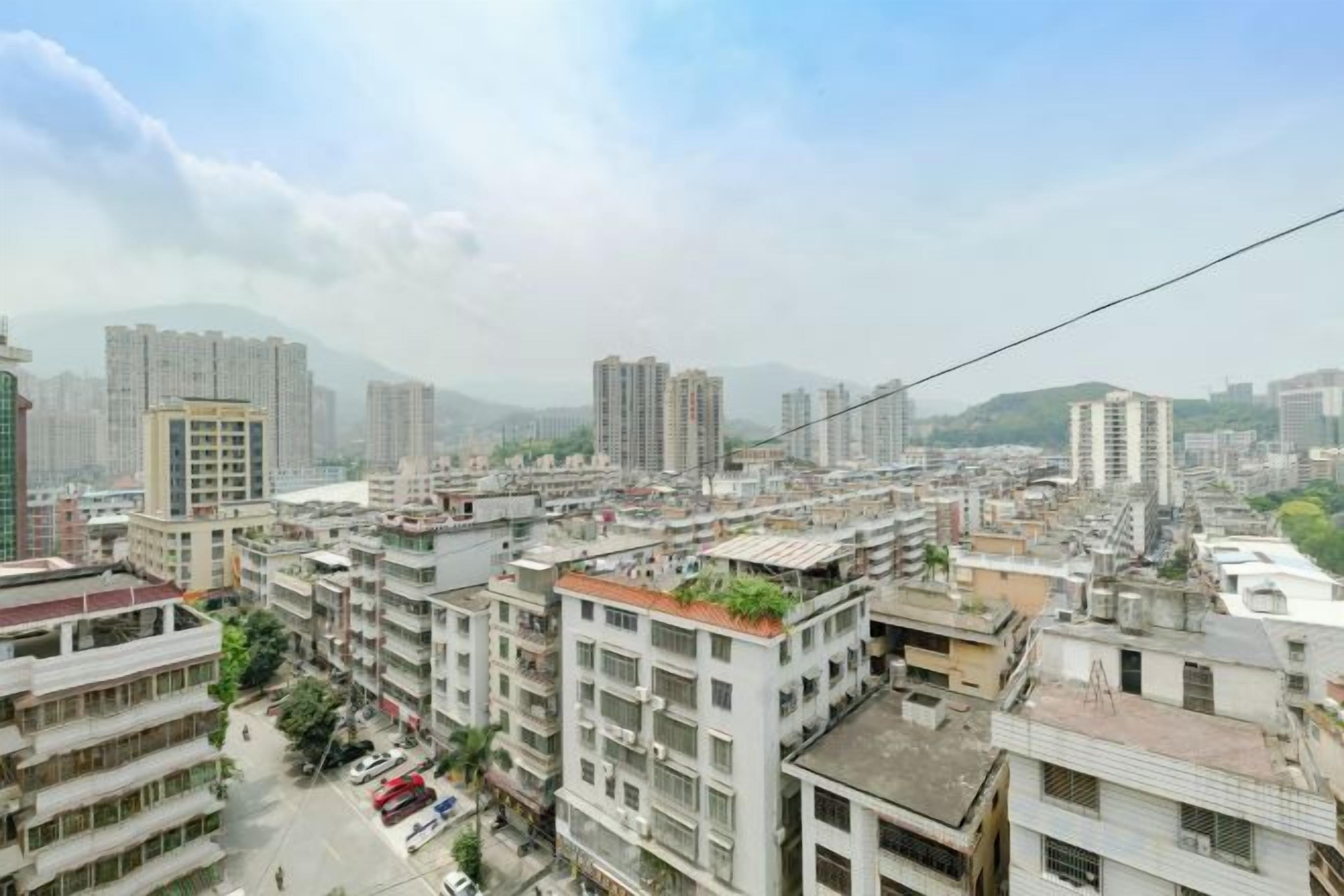 Une vue urbaine avec de hauts immeubles, un ciel dégagé et une chaîne de montagnes à l’horizon.