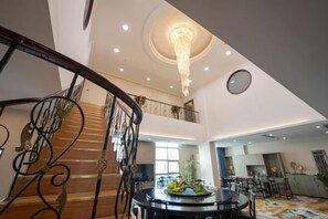Un'ampia hall con una scalinata monumentale, un lampadario e un tavolo da pranzo rotondo con sedie.