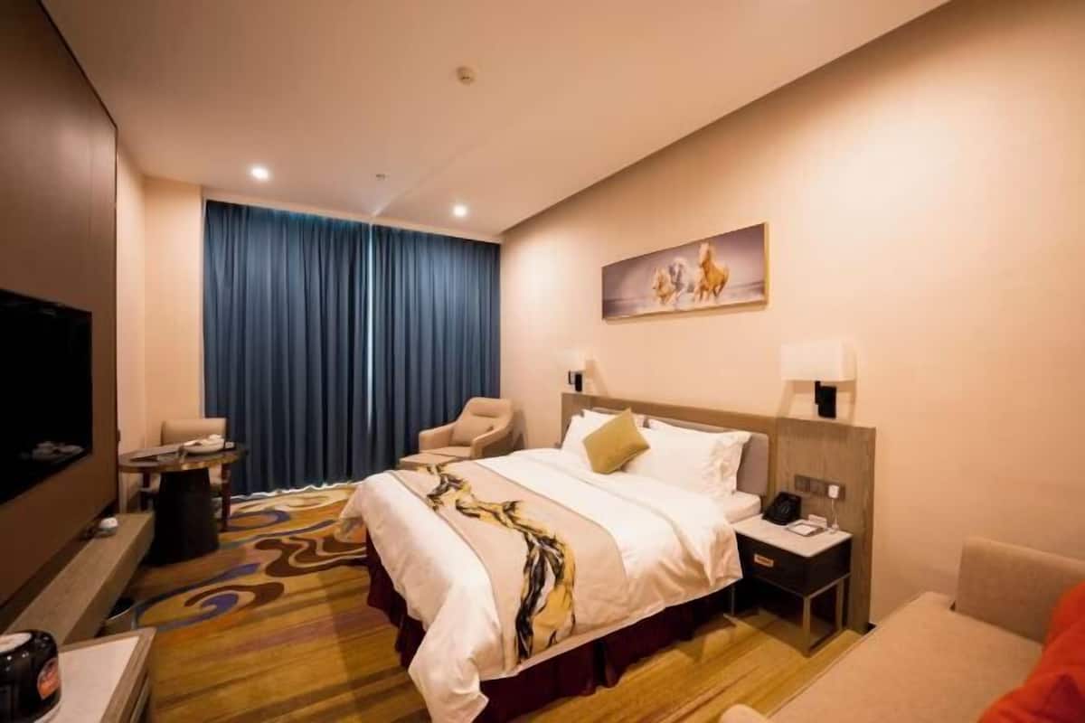 A hotel room with a bed, a desk, a chair, a TV, and a painting on the wall.