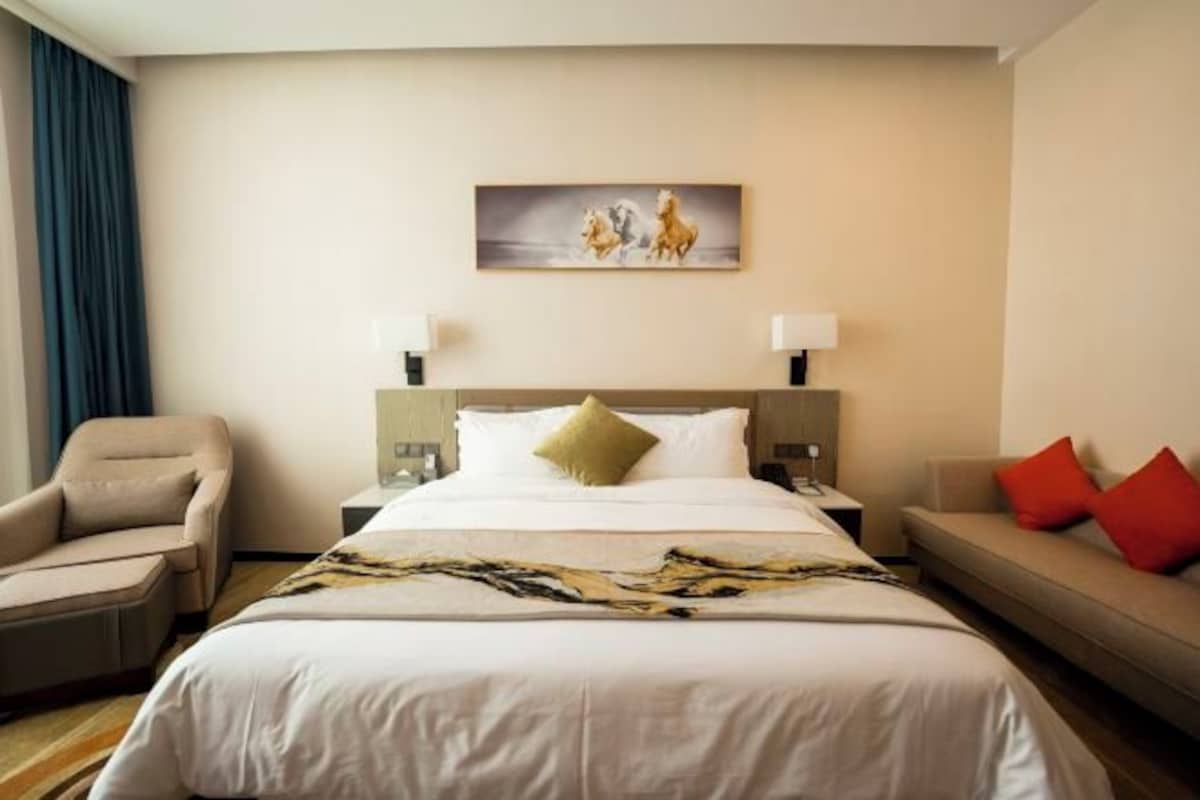 Una habitación de hotel con una cama, una silla, un sofá, un cuadro en la pared y dos lámparas de noche.
