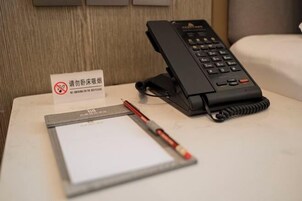 Una habitación de hotel con un teléfono, un bloc de notas y un bolígrafo sobre una mesita.