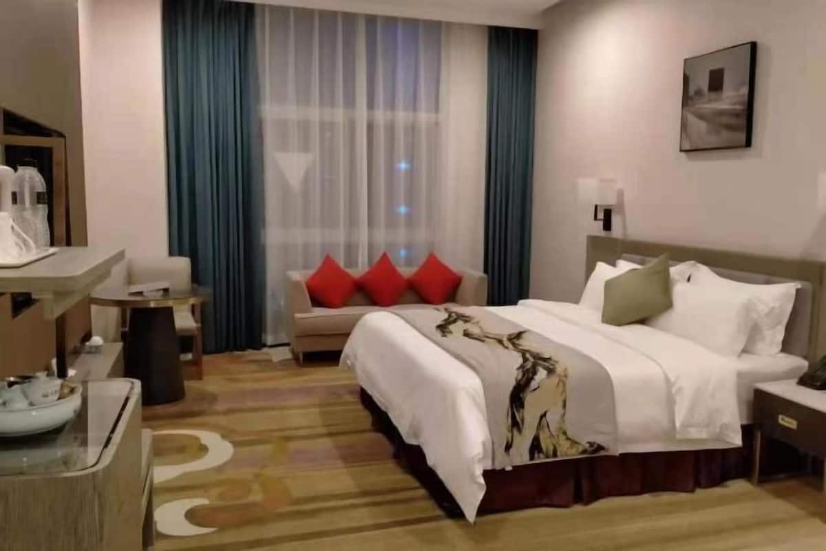 A hotel room with a bed, a desk, a chair, a coffee machine, and a window with curtains.