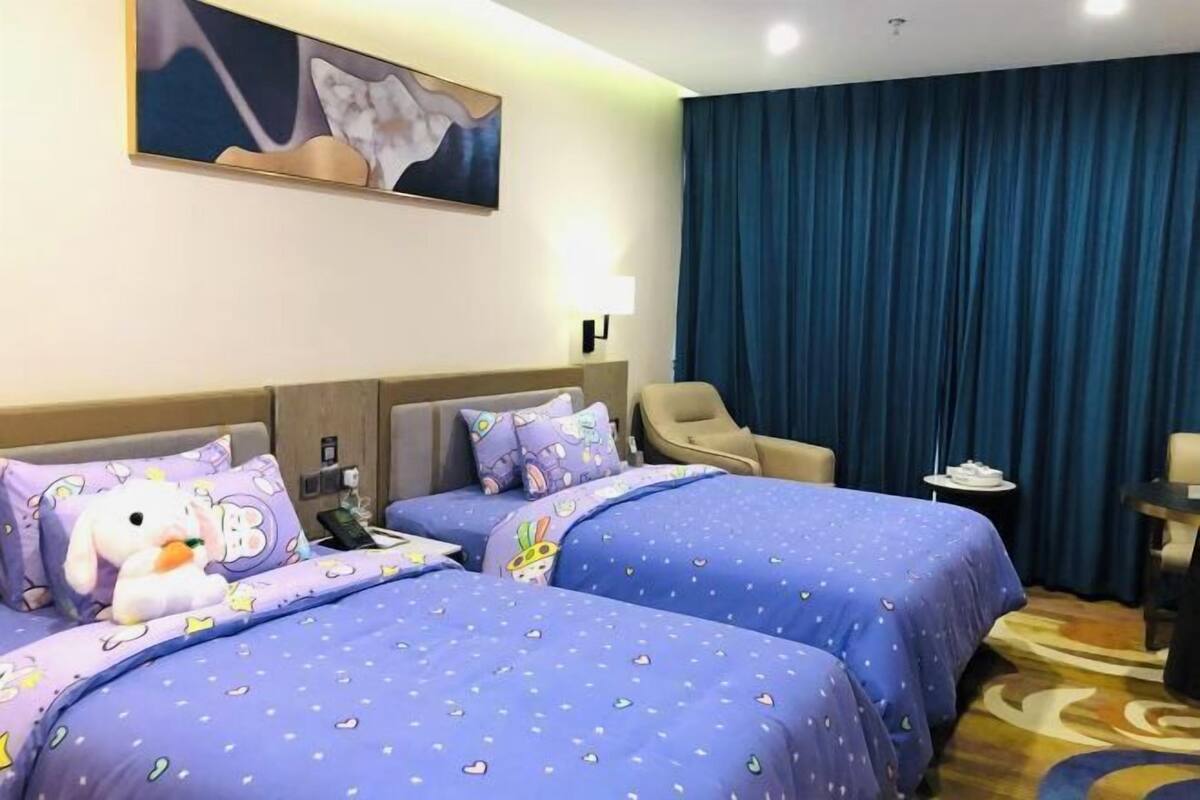 A hotel room with two beds, a chair, a desk, and a painting on the wall.