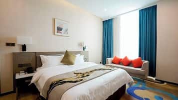 A hotel room with a bed, a nightstand, a sofa, a window with curtains, and a painting on the wall.