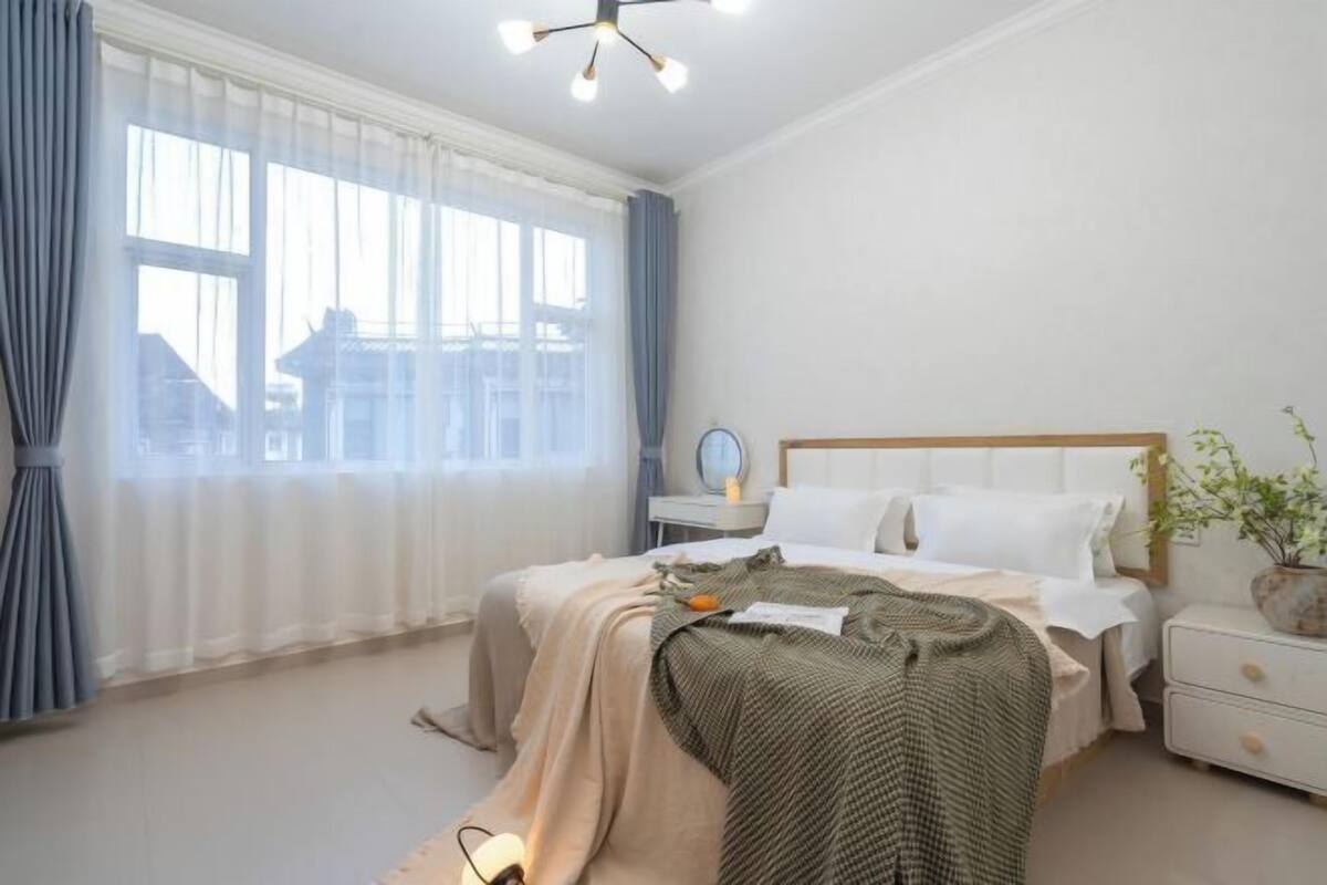 Une chambre à coucher avec un lit, une table de chevet, une lampe et une fenêtre avec des rideaux.