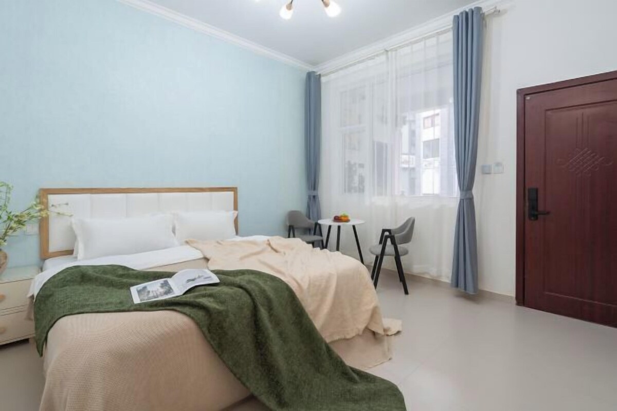 A bedroom with a bed, bedside table, lamp, and a window with curtains.